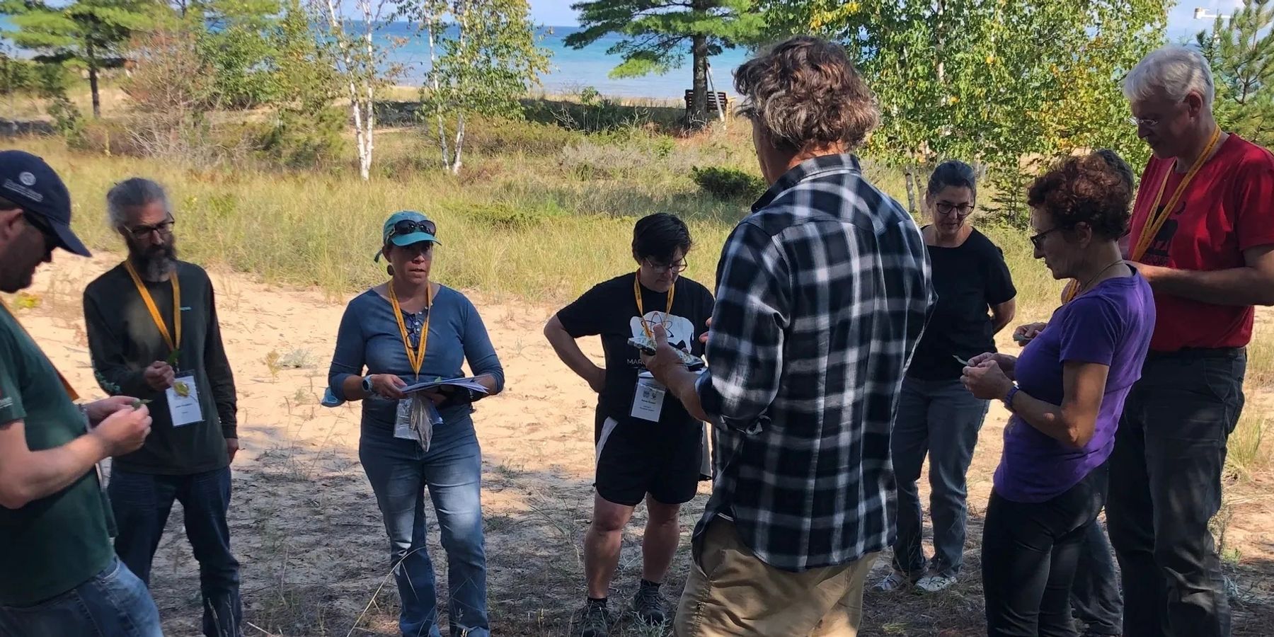 Rich standing with a group of adults in a clearing by the water, leading a field session.
